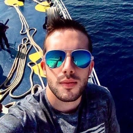 Person on a boat deck with neatly coiled ropes and clear blue water in the background.